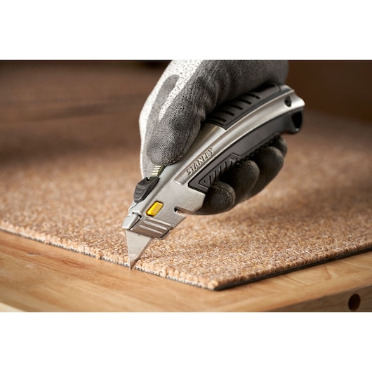 Photo of STANLEY 0-10-788 utility knife cutting carpet, held by gloved hand.