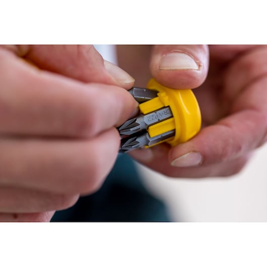 Photo of hands holding STANLEY 0-66-358 rotary bit holder, yellow handle showing bit storage close-up.