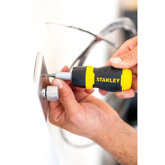 Photo of STANLEY 0-66-358 stubby screwdriver with black and yellow handle used to tighten a screw on a metal plate.