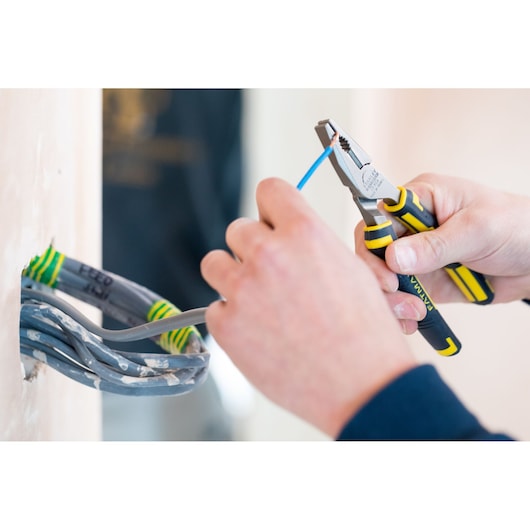 STANLEY 0-89-866 pliers used to strip blue wire near wall socket, close-up indoor scene.