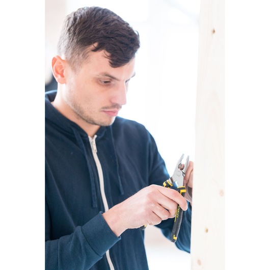 Photo of STANLEY 0-89-866 pliers with black and yellow handles in use near light wood panel.