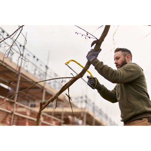 STANLEY 1-20-447 bow saw cutting tree branch outdoors near construction site.