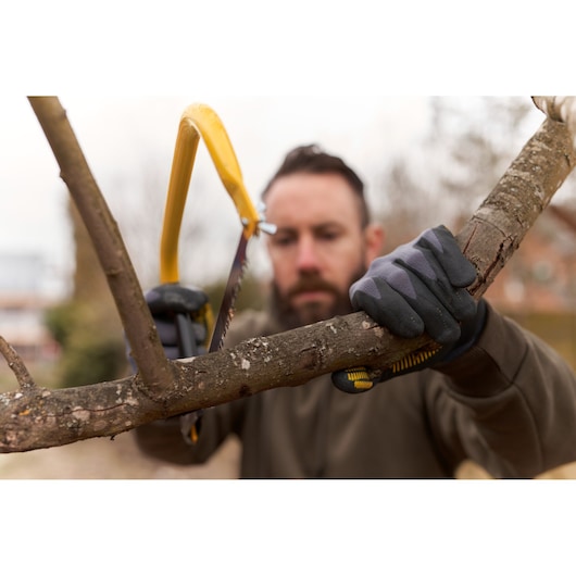 STANLEY 1-20-447 bow saw with yellow frame cutting a tree branch outdoors, gloves visible on hands.