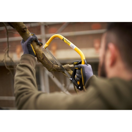STANLEY 1-20-447 hand saw with yellow frame cutting tree branch, close-up outdoor use.
