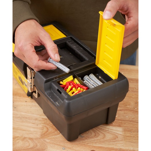 STANLEY 1-92-064 tool box with yellow lid, holding assorted wall plugs on a wood surface, close-up angle
