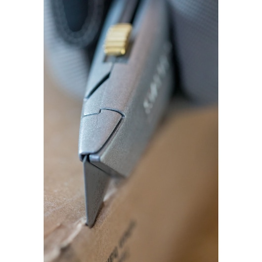 STANLEY 2-10-099 utility knife close-up cutting cardboard, silver body, gold slider, photography.