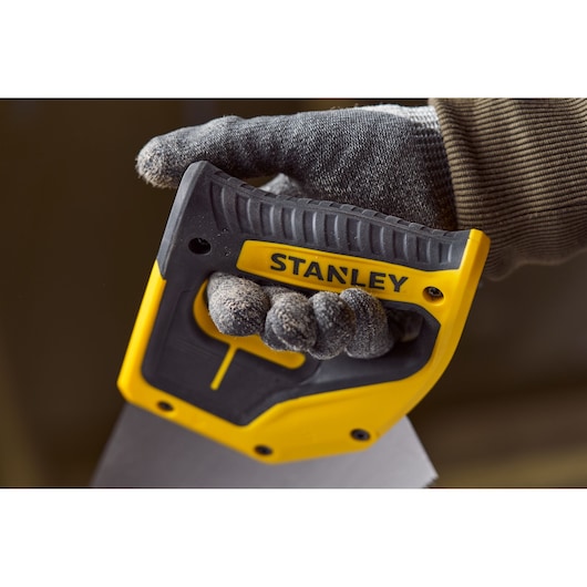 Close-up of STANLEY 2-15-288 hand saw handle with yellow and black grip, held by a gloved hand.