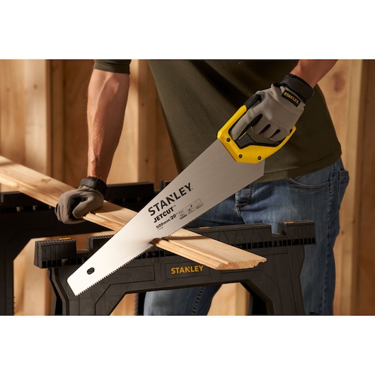 Photo of STANLEY 2-15-599 hand saw cutting wood on sawhorse, closeup of blade and yellow handle.