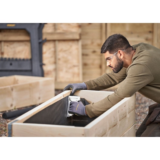 STANLEY 6-TR45 staple gun used by a person wearing gloves to assemble a wooden planter, outdoor setting.