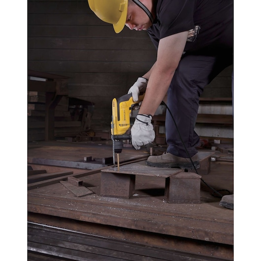 Photo of STANLEY SDH700CK corded drill in use, drilling metal in an industrial workshop.