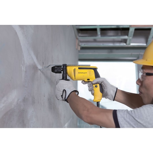 Stanley SDH700CK yellow corded hammer drill used on wall by gloved hands, side angle.
