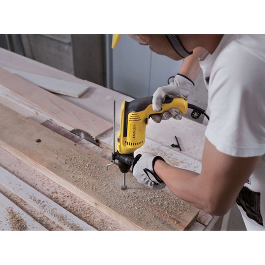 STANLEY SDH700CK yellow drill used on wood plank by gloved hand, workshop setting.