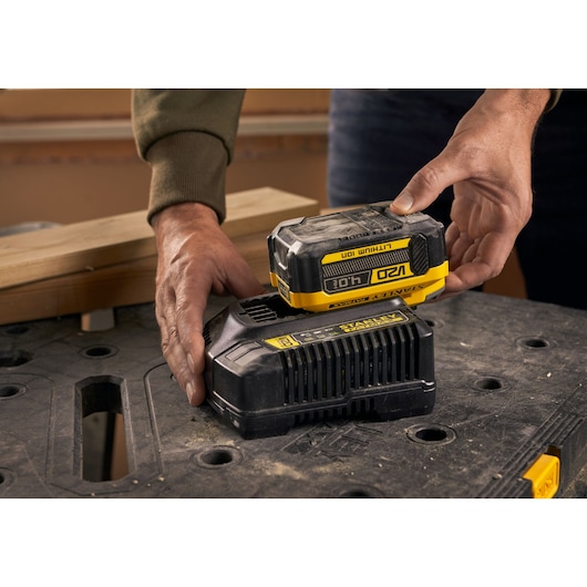 Photo of STANLEY SFMCB204 battery being placed on charger on workshop table.