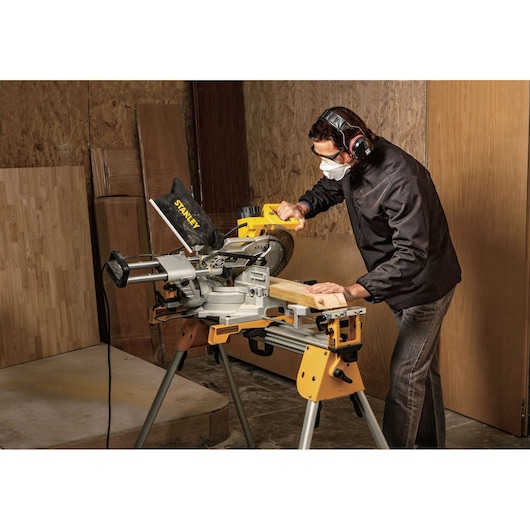STANLEY SM18-B2C miter saw in use, cutting wood in a workshop setting, operator wearing ear protection.