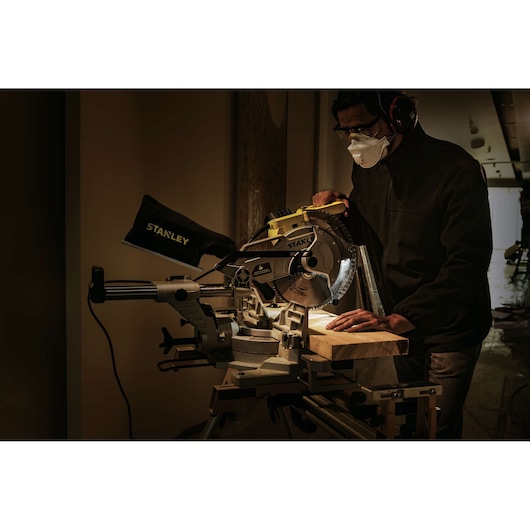 STANLEY SM18-B2C sliding miter saw in use cutting wood, operator wearing safety gear, workshop scene.