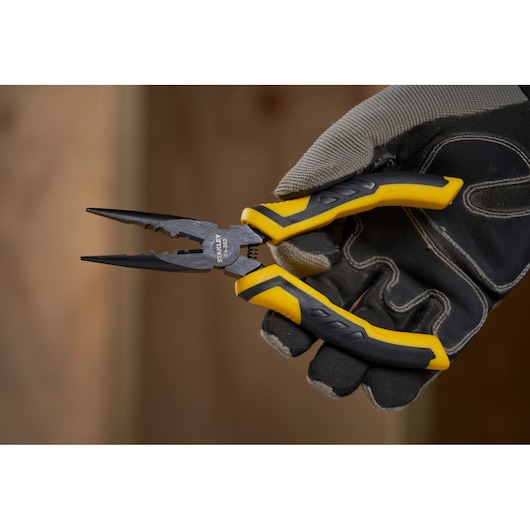 STANLEY STHT0-74364 pliers with yellow and black handles held in a gloved hand, close-up side angle.