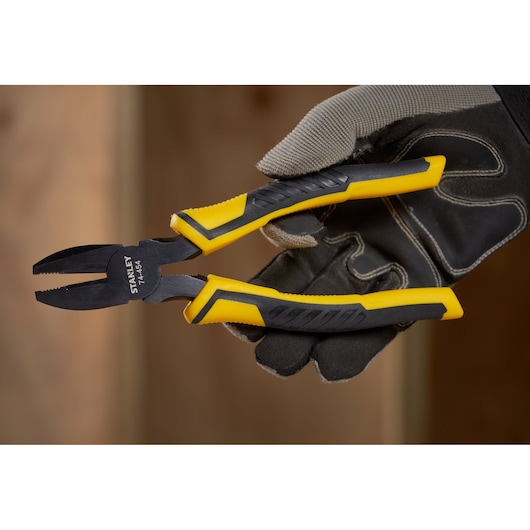 Photo of STANLEY STHT0-74456 combination pliers with yellow and black ergonomic grip, held by gloved hand.